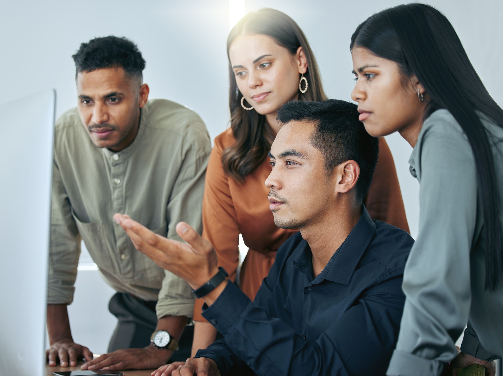 Shot of a diverse group of businesspeople standing together in the office and using a computer